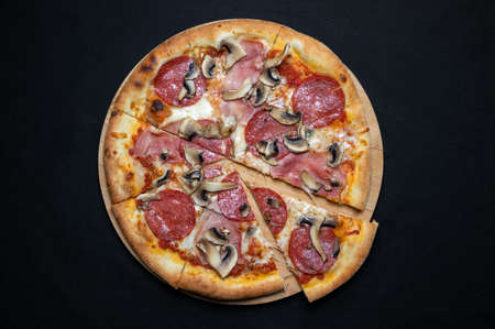 Pizza with tomato sauce, mozzarella, salami and mushrooms on a black background.の写真素材