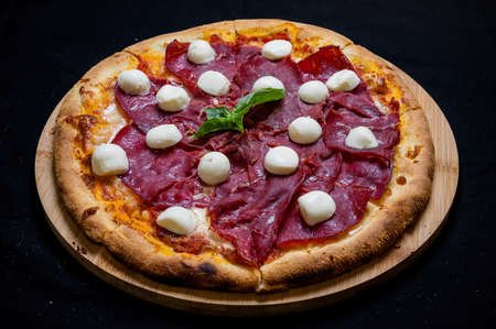 Pizza with tomato sauce, mozzarella and smoked ham on a black background.の写真素材