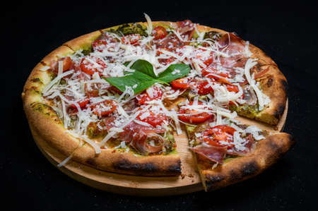 Pizza with tomato sauce, smoked pork ham, avocado sauce, mozzarella and cherry tomatoes on a black background.の写真素材