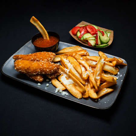 Crispy menu with french fries, chili sauce, and vegetable salad on a black backgroundの写真素材