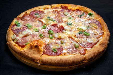 Pizza with green onions, salami, ham, mozzarella and tomato sauce on a black background.の写真素材