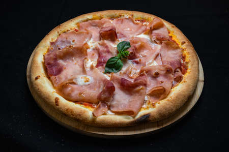 Pizza with tomato sauce, mozzarella and ham on a black background.の写真素材