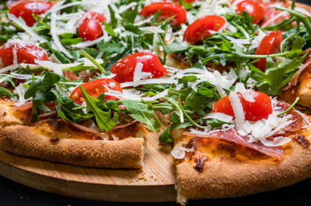 Pizza with tomato sauce, smoked pork muscles, mozzarella, arugula salad and cherry tomatoes on a black background.の写真素材