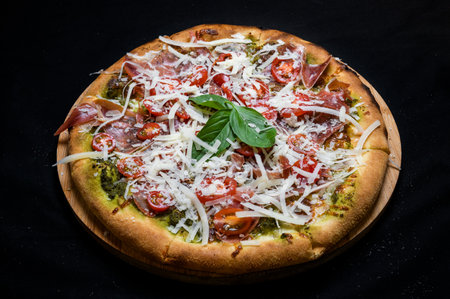 Pizza with tomato sauce, smoked pork ham, avocado sauce, mozzarella and cherry tomatoes on a black background.の写真素材