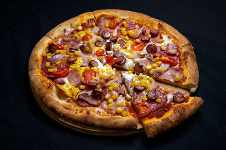 Pizza with tomato sauce, mozzarella, sour cream, salami, pork ham, sausages, corn and cherry tomatoes on a black backgroundの写真素材