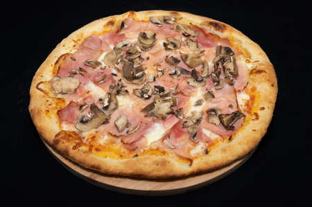 Pizza with tomato sauce, salami, pork ham, olives, peppers and mushrooms on a black background.の写真素材