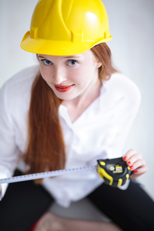 Long haired red headed woman holding a tape measure and wearing a safety hatの写真素材
