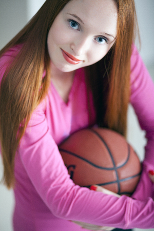Attractive long haired holding a basketball ball and sitting on floorの写真素材