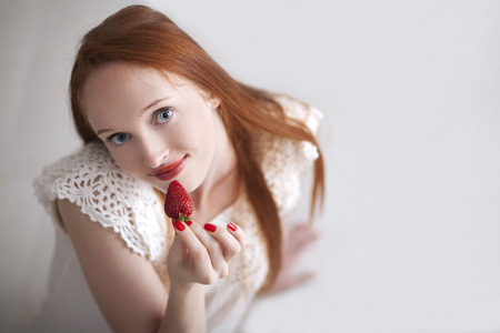 Young beautiful long haired woman holding a strawberry and smilingの写真素材