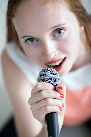 Attractive long haired young woman singing with a microphone and sitting on floorの写真素材