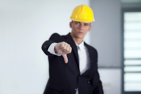 Successful businessman with yellow helmet poses and hand gesturing thumbs downの写真素材