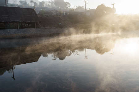 Mist on village at dawn with clouds reflected in the calm waterの写真素材