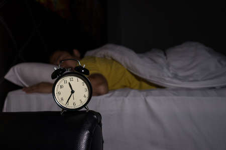 Alarm clock at 11:35 pm on bedside table in bed male sleeping in background, man rest in dark room at nightの写真素材