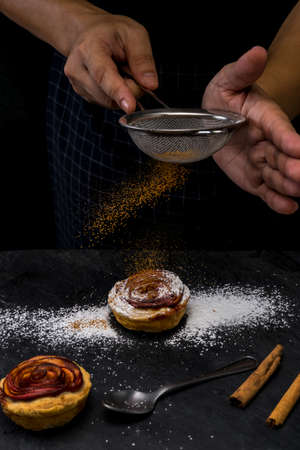 action of hand chef sprinkle ground cinnamon on pie apple rose form. dark food mood toneの写真素材