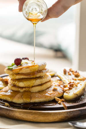 hand pouring maple syrup on pancake and bananaの写真素材