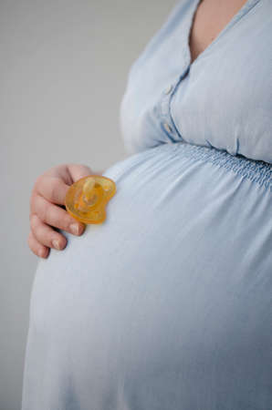 detail of pregnant woman in light blue denim dress holding pacifierの写真素材