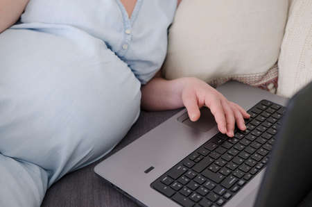 pregnant woman in light blue denim dress working on laptop at homeの写真素材