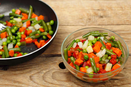 bowl of vegetable salad in front of frying panの写真素材