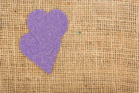 two purple glossy hearts on burlap textureの写真素材