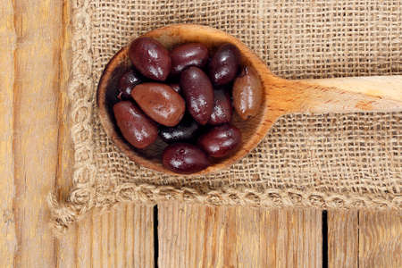 brown olives in wooden ladle on burlap textureの写真素材