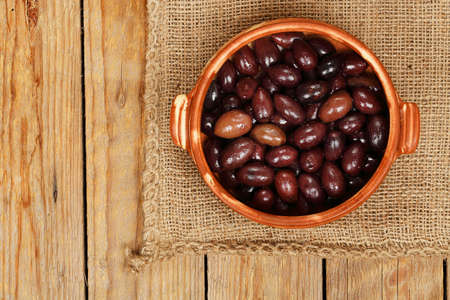 brown olives in clay bowl on burlap textureの写真素材