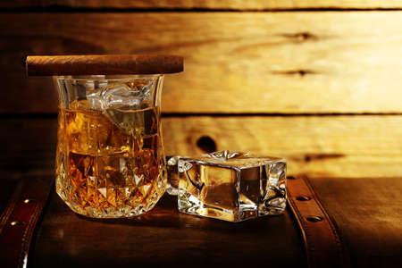 elegant glass of whiskey on the rocks on an old chest, against wooden surfaceの写真素材