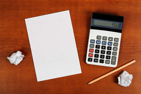 calculator, blank notepad and pencil on wooden desk