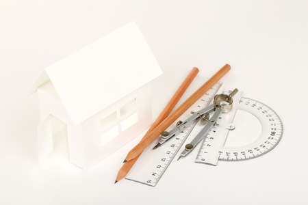 white cardboard house with pencils, rulers and compasses on whiteの写真素材