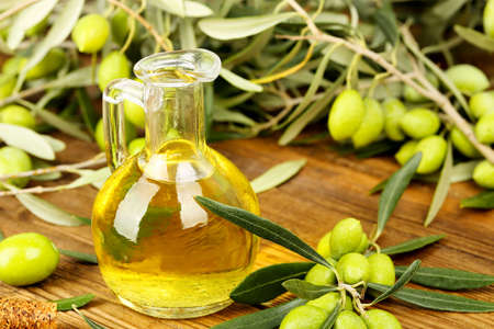 jug of olive oil and olive tree branches on old wooden tableの写真素材