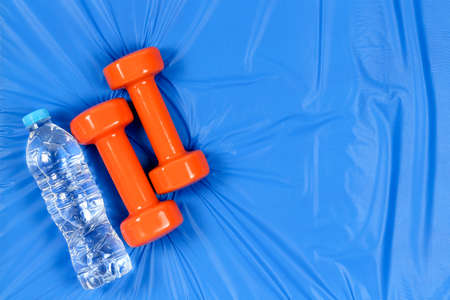 orange dumbbells and water on blue mat with copy  space