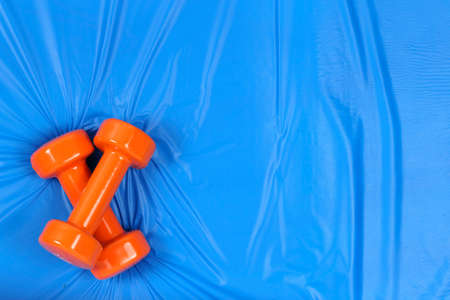orange dumbbells and water on blue mat with copy  space