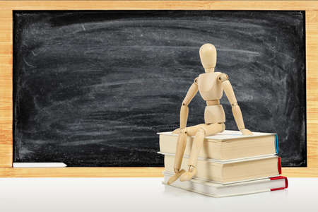 wooden dummy sitting on books against blackboard, education concept
