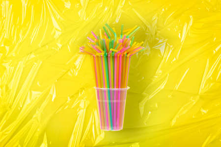 plastic drinking straws in plastic cup on yellow background