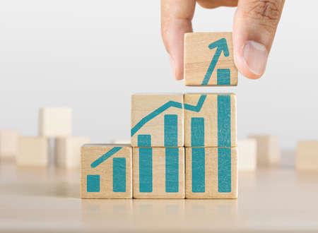 Business growth, progress or success concept. Wooden blocks with a growing bar chart graphic arranged in stair shape and a man is holding the top one.の写真素材