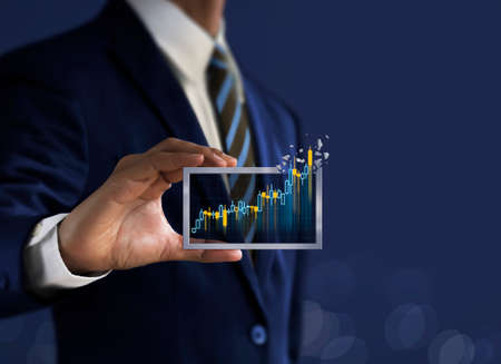 Business growth, progress or success concept. Businessman is holding a growing virtual hologram candlestick chart on dark blue background.の写真素材
