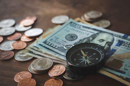 Financial, banking or investment concept. Dollar banknotes, coins and compass on wood desk background with copy space.の写真素材
