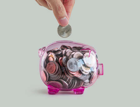 Money savings, business growth or financial concept. Hand putting a coin into  pink piggy bank on white background.の写真素材