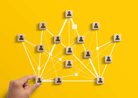 Human resources management, teamwork management or business strategy to success concept. Hand is arranging wooden blocks with human icon in polygon crown shape network on yellow background.の写真素材