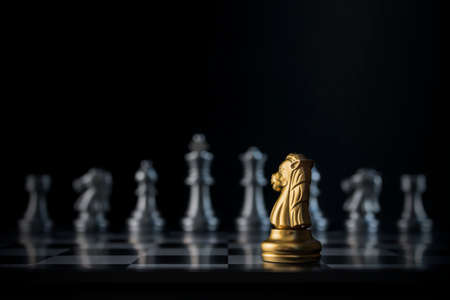 Golden chess knight is facing the silver opponent chess on black background. Leader, leadership, business strategy, challenge, brave or fearless concept.の写真素材