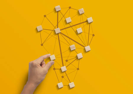 Business strategy, business management or business success concept. Hand is arranging wooden blocks in low polygon light bulb shape network on yellow background.の写真素材