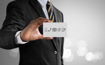 Customer service, call center service or contact us concept Businessman holding communication icons (mobile phone, telephone, mail, email, social media) card on bright tone background.の写真素材