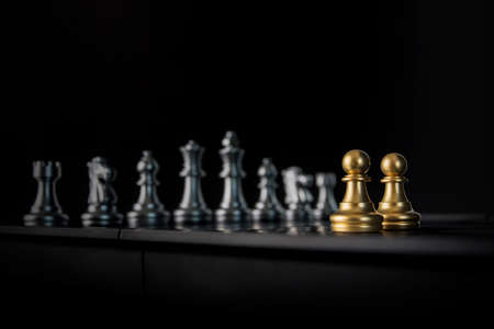 Two golden chess pawns are facing silver chess on black background. Business partnership concept.の写真素材