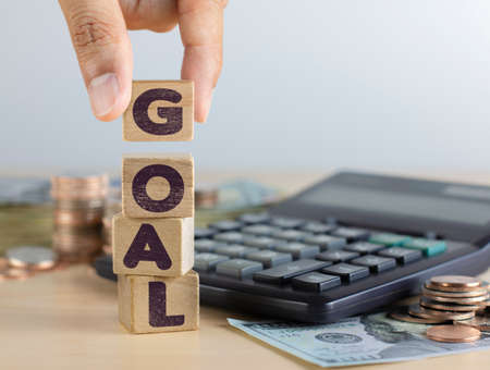 Hand arranging wooden blocks with the word GOAL in front of calculator and money. Goal, success or business concept.の写真素材