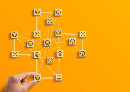 Positive attitude, customer satisfaction, emotion management or happiness concept. Hand is arranging wooden blocks with happy face emoji icon in polygon plus shape network on yellow background.の写真素材