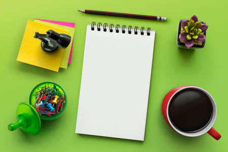 Notebook on office table with a cup of coffee, plant, stationery and office supplies. Blank notepad paper for input copy or text. Top view desk, flat lay green color background concept.の写真素材