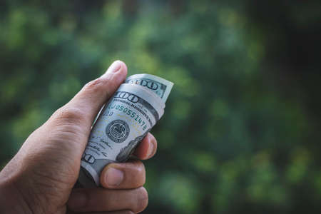 Financial concept, earning concept or donation concept. A roll of US dollar banknotes in hand.の写真素材