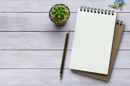 Notebook on white wooden table with a plant, paper clip and pencil. Blank notepad paper for input copy or text. Top view desk, flat lay white background concept.の写真素材
