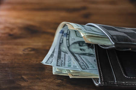 Financial concept. A close-up of many hundred dollar banknotes in wallet on wooden desk background with copy space.の写真素材