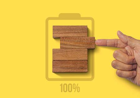 Fully charged, recharge, reboot, refresh or mindset concept. Hand putting wooden blocks with the battery charger and 100% icon on yellow background.の写真素材