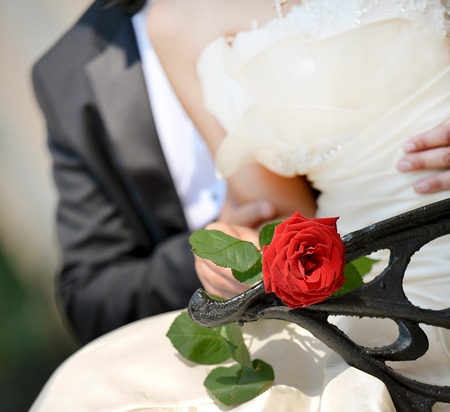 Lovely Wedding Couple sitting on a bench with a red roseの写真素材